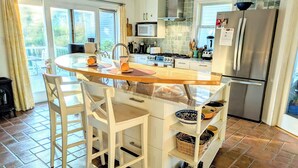 Une cuisine dotée d’un îlot central, de meubles blancs et d’un réfrigérateur en acier inoxydable, ainsi que d’une fenêtre donnant sur un balcon.