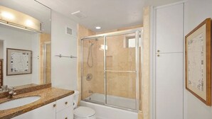 A modern bathroom with a glass-enclosed shower, a white toilet, and a granite countertop sink.