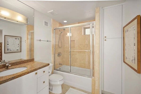A modern bathroom with a glass-enclosed shower, a white toilet, and a granite countertop sink.