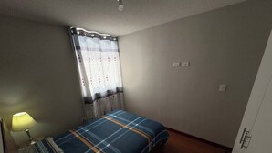 A bedroom with a bed, a nightstand, a lamp, a window with curtains, and a door. - In condominium with beautiful views (José Luis Bustamante y Rivero)