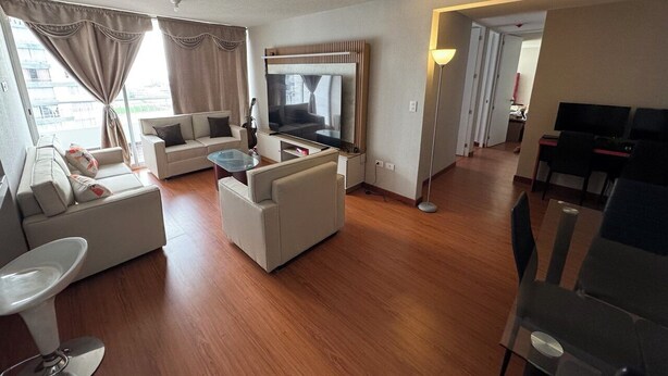 A modern living room with a sofa set, a TV, and a dining area with chairs and a table. - In condominium with beautiful views (José Luis Bustamante y Rivero)