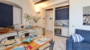 A compact kitchen with a microwave, sink, and stove. There is a dining area with a table set for two, chairs, and a blue sofa. - 1 bedroom awesome apartment in Sestri Levante (Sestri Levante)