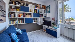 A living room with a blue sofa, a TV stand with a flat-screen TV, and a bookshelf filled with books and decorative items. - 1 bedroom awesome apartment in Sestri Levante (Sestri Levante)