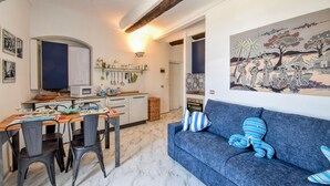 A cozy living room with a blue sofa, a dining area with a wooden table and chairs, and a kitchen with white cabinets and a hanging pot rack. - 1 bedroom awesome apartment in Sestri Levante (Sestri Levante)