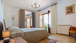 Un dormitorio con una cama, una lámpara, una silla, un radiador y un cuadro en la pared.
