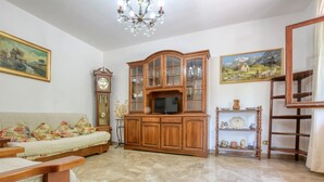 Una sala de estar con un sofá, un aparador de madera con puertas de vidrio, un reloj y un televisor.