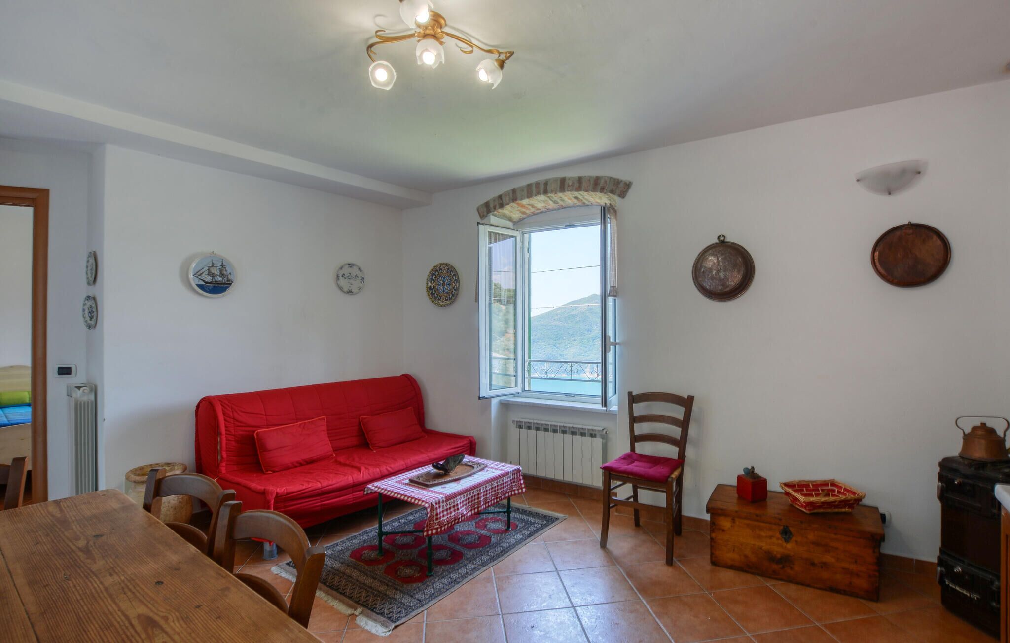 Un salón acogedor con un sofá rojo, una mesa de madera y una ventana con vistas a las colinas.