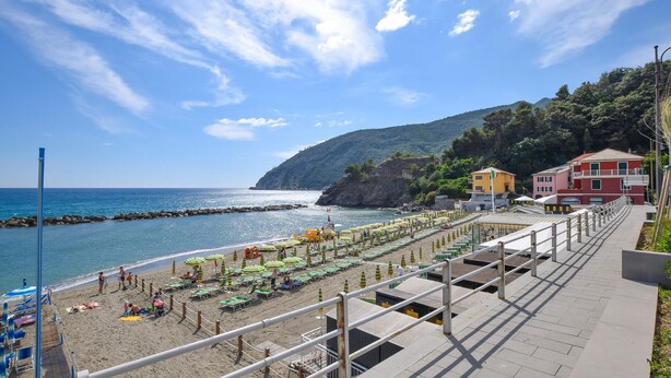 A coastal beach with rows of beach umbrellas and sun loungers, a promenade with railings, and buildings in the background. - Pet friendly apartment in Moneglia with WiFi (Moneglia)