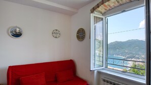 A room with a red sofa, a window with a view of a coastal landscape, and three decorative plates on the wall. - Pet friendly apartment in Moneglia with WiFi (Moneglia)