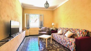 A small living room with a sofa, a chair, a television, a lamp, and a window with a view of a street. - 2 bedroom stunning apartment in Taggia (Taggia)