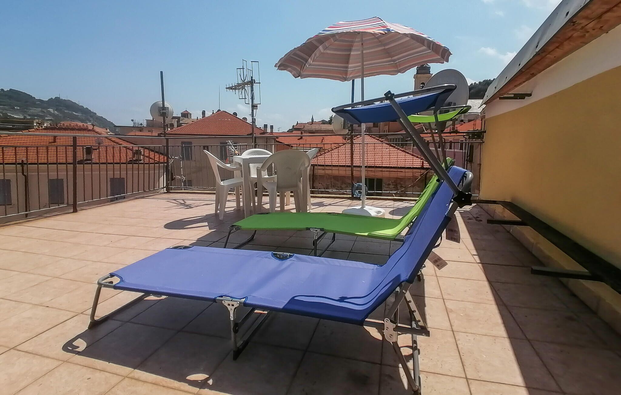 A rooftop terrace with a sunbed, a table with chairs, and a striped umbrella.