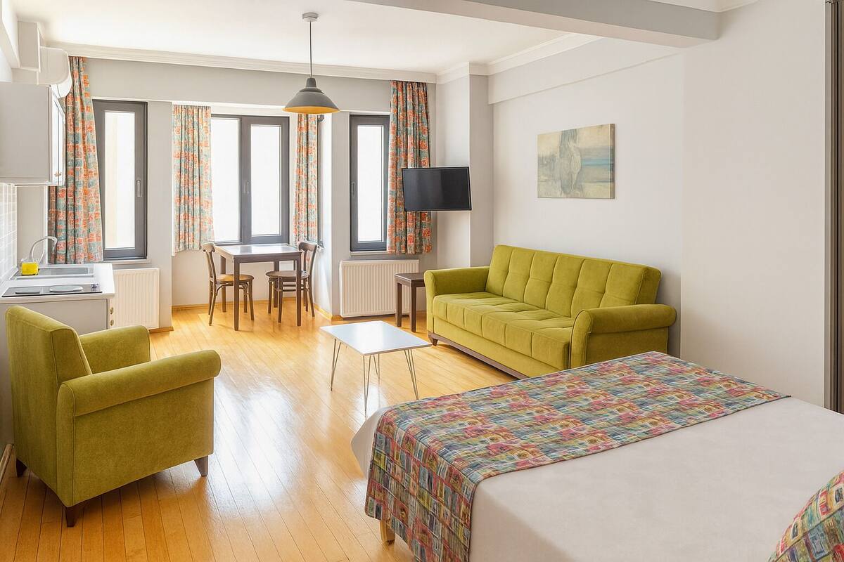 A hotel room with a bed, a sofa, a dining table with chairs, a TV, and a window with curtains.