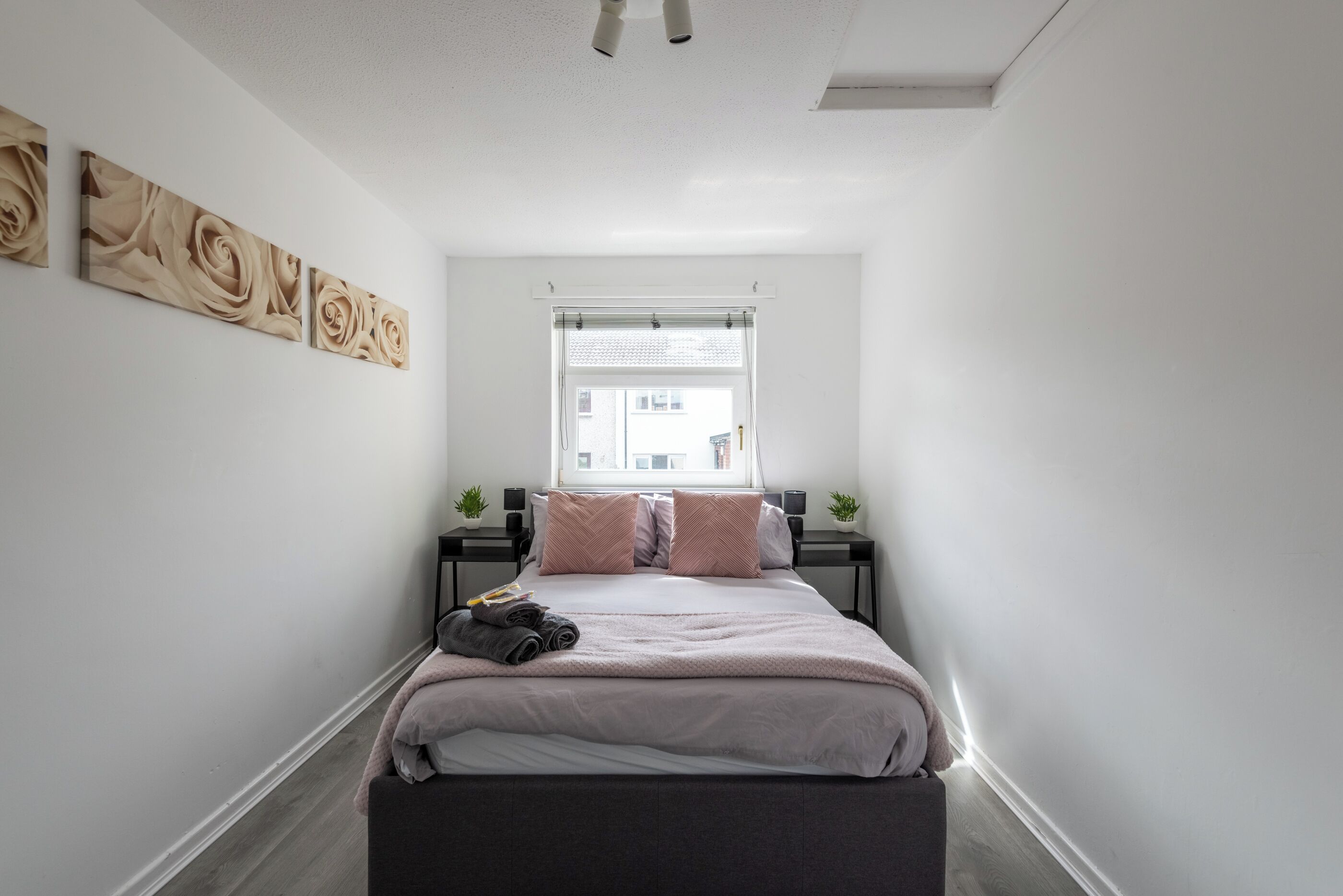 Un dormitorio con cama, ventana, mesita de noche y decoración en la pared.