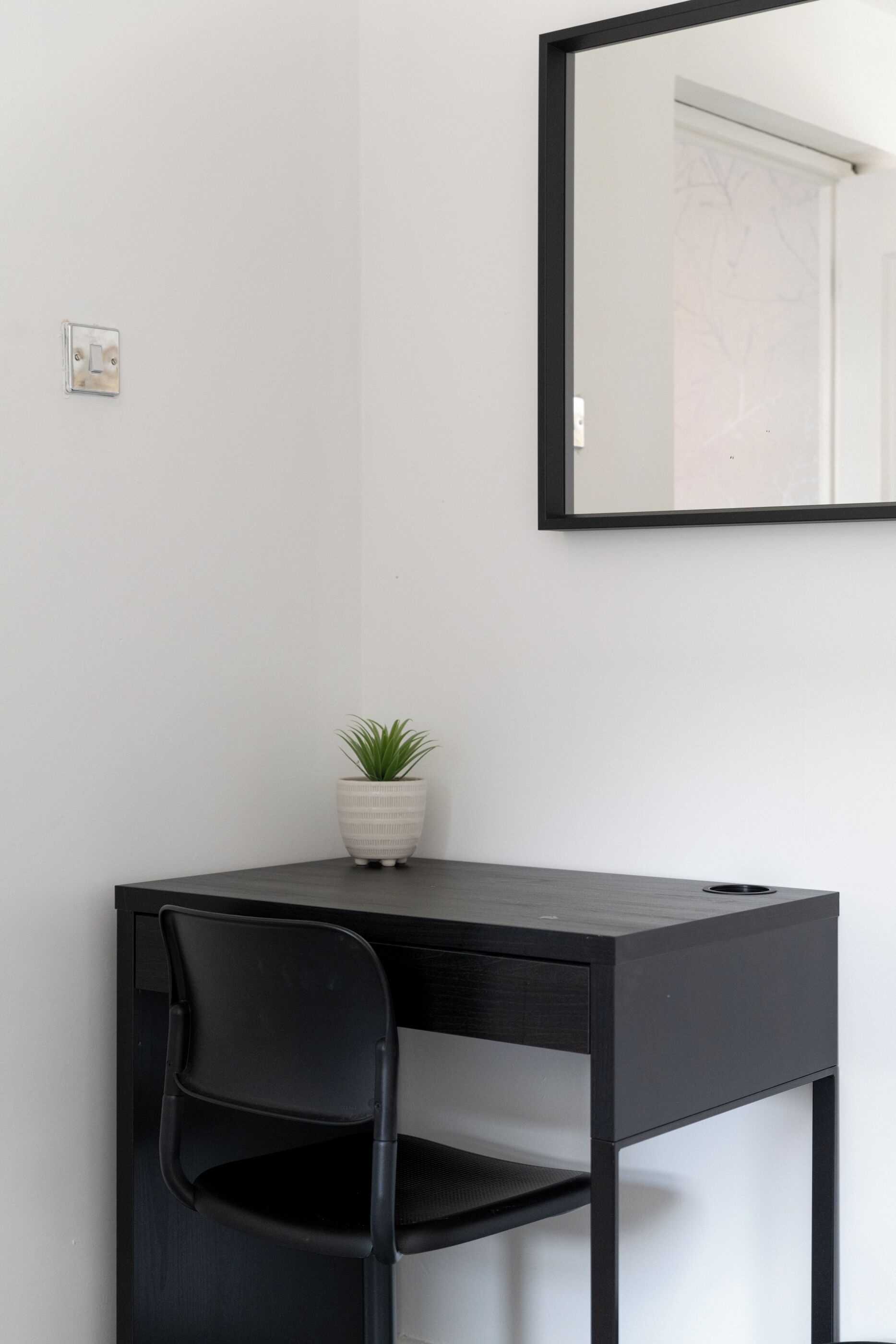 Una habitación minimalista con un escritorio, una silla y una planta en maceta.