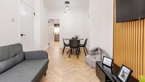 A modern living room with a grey sofa, a bean bag, a dining table with chairs, and a TV mounted on a wooden panel. - Modern 2-bed home with free on-street parking, fast Wi-Fi & family amenities. (Belfast)