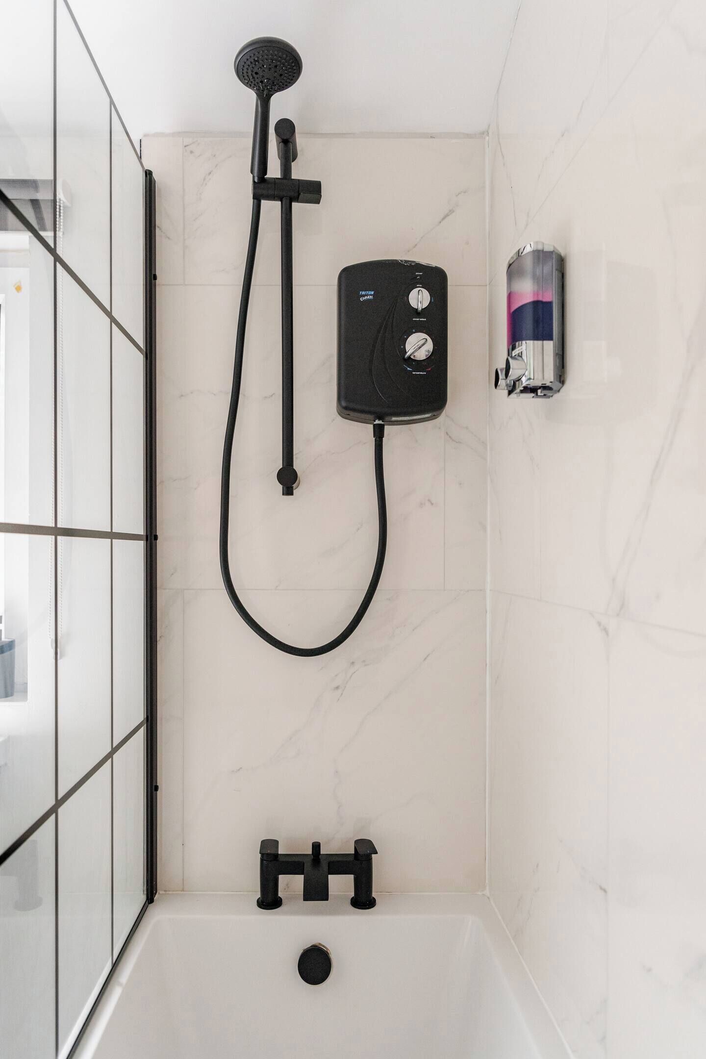 Une salle de bain moderne dotée d’une douche à parois de verre, d’un pommeau de douche à main, d’un panneau de commande mural et d’une baignoire intégrée.