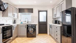 A modern kitchen with a built-in washing machine, a refrigerator, and a microwave. - Modern 2-bed home with free on-street parking, fast Wi-Fi & family amenities. (Belfast)