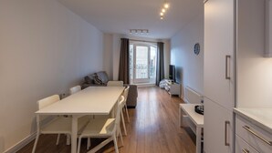 A modern, well-lit room with a dining table, chairs, a sofa, and a TV.