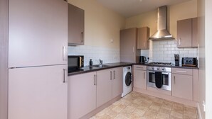 Une cuisine moderne dotée d’appareils électroménagers en acier inoxydable, d’un lave-linge et d’un revêtement mural en carreaux.