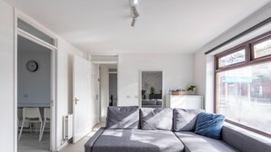 Una sala de estar moderna con un sofá seccional gris, una puerta blanca y un amplio ventanal con vista a la calle.