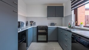 Una cocina moderna con gabinetes grises, horno integrado, lavavajillas y una ventana con vista a un muro de ladrillo.