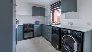Una cocina compacta con gabinetes grises, horno empotrado, lavavajillas y una ventana con persianas.