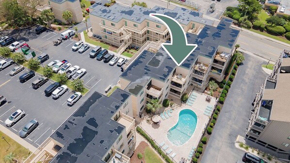 Vista aérea de um edifício residencial de vários andares com estacionamento, piscina e área ajardinada.