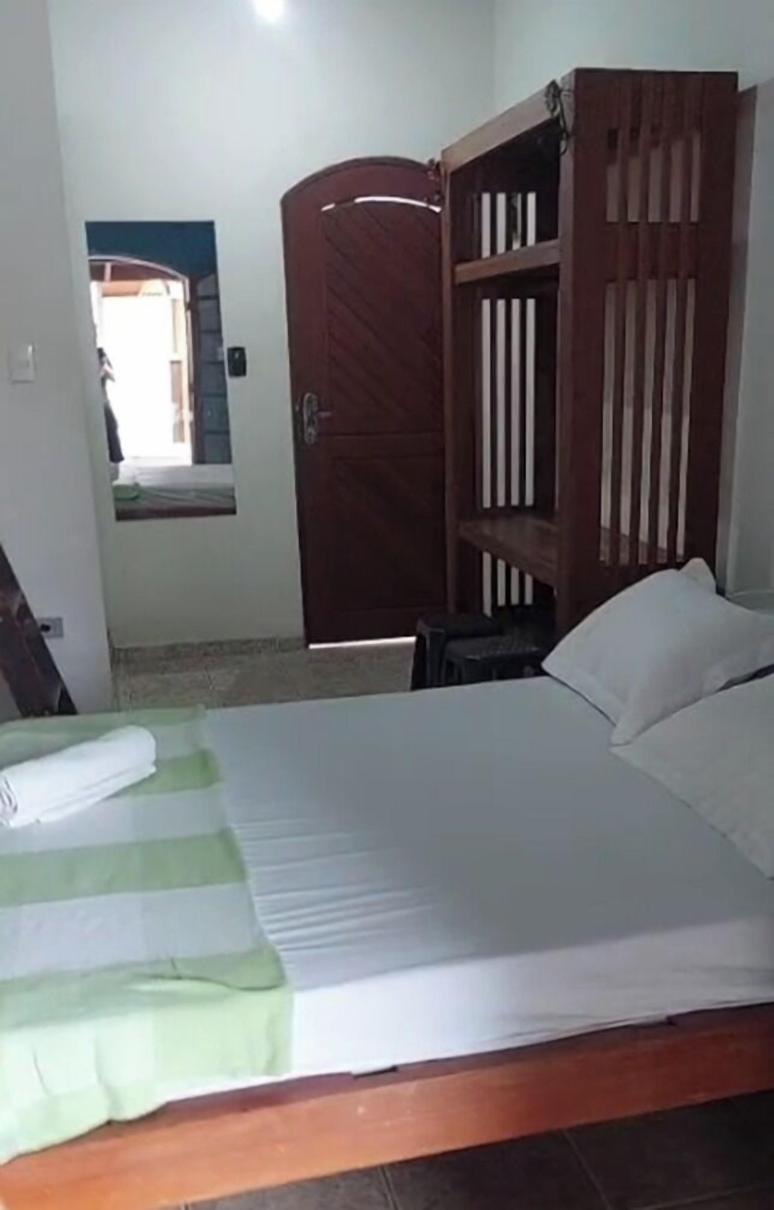A room with a bed, a wooden wardrobe, and a small table.