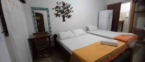 A room with two beds, a desk, a chair, a refrigerator, and a wall decoration.