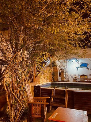 An outdoor seating area with wooden tables and chairs, a tiled pool, and a mural of a blue fish on the wall. - La Civetta Maresias Pousada e Holtel (São Sebastião)
