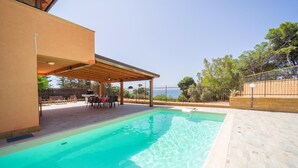 Una piscina con cubierta de madera, un porche techado y vista al mar.