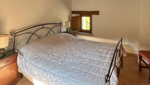 A bedroom with a bed, a nightstand, a lamp, a window, and a wooden bench.