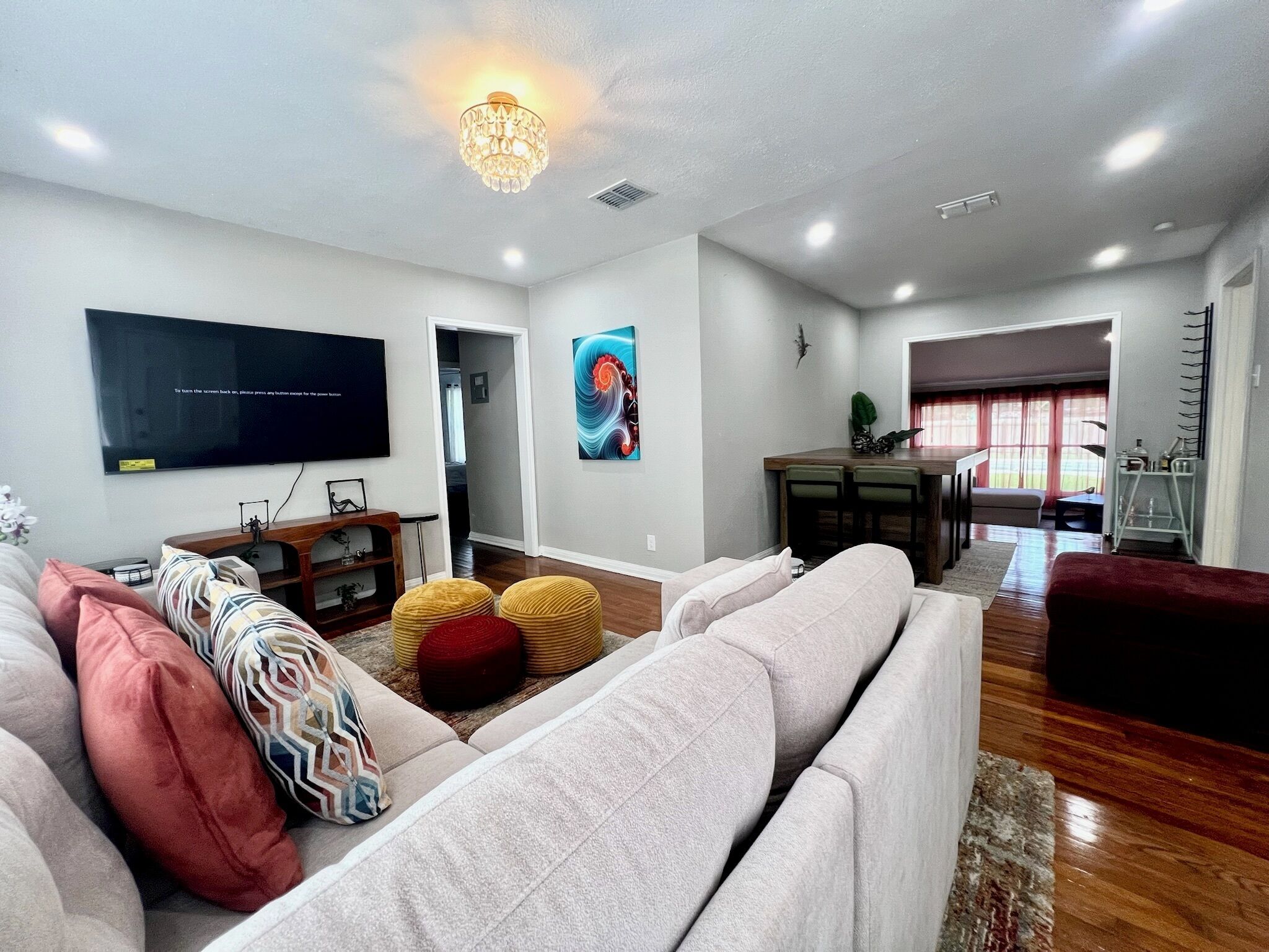 A modern living room with a flat-screen TV, a chandelier, and a dining area with a view.