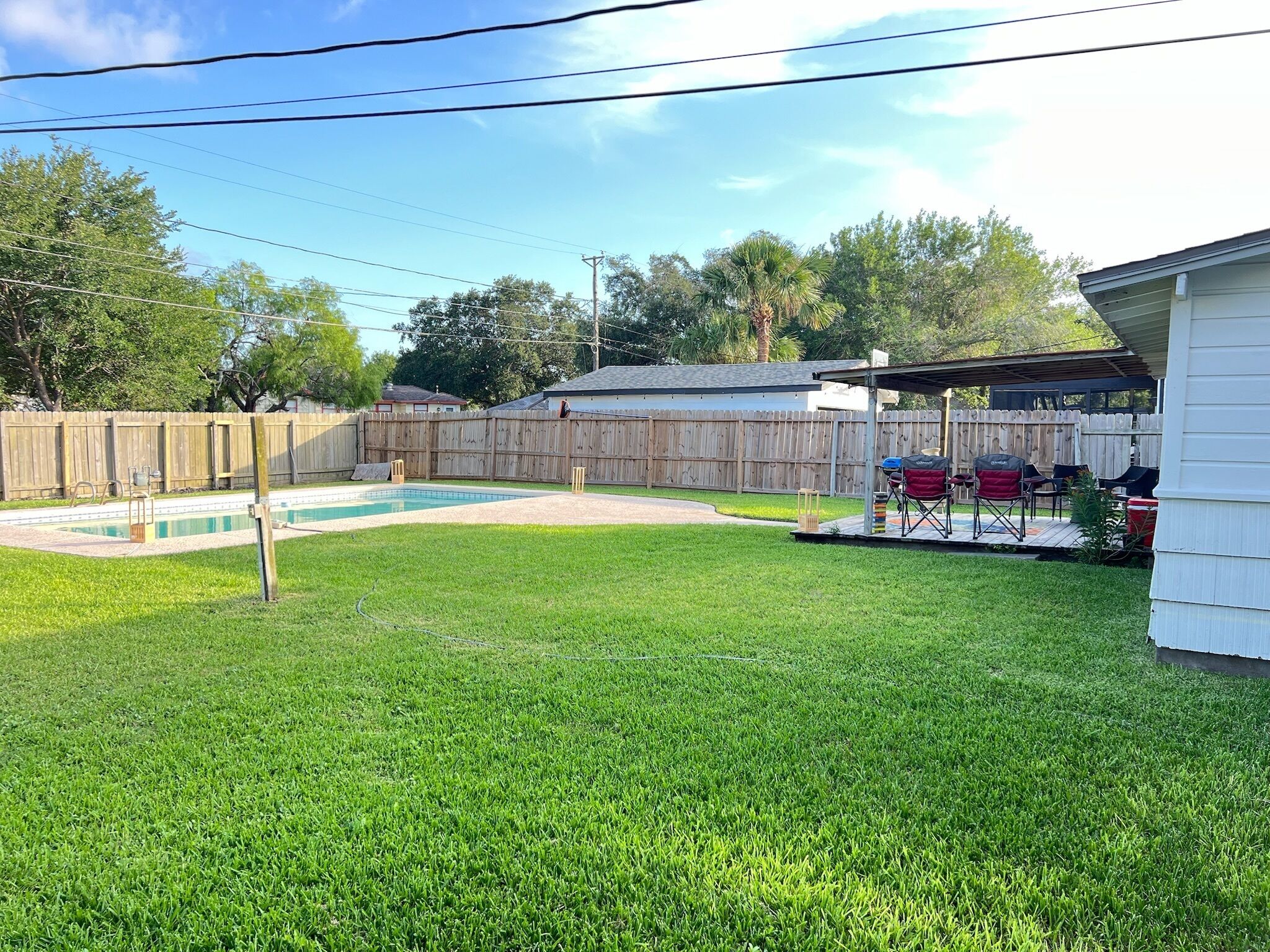 A backyard with a swimming pool, a wooden fence, and a barbecue area.