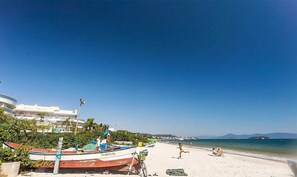 Une plage avec des bateaux, un ciel dégagé et un bâtiment en arrière-plan.