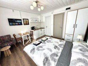 A compact room with a bed, a small desk, a chair, a sofa, a kitchenette, and a wardrobe.
