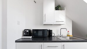 Eine moderne Küche mit weißen Schränken, einer schwarzen Arbeitsplatte, einer Mikrowelle, einer Kaffeemaschine und einem Spülbecken mit Armatur.