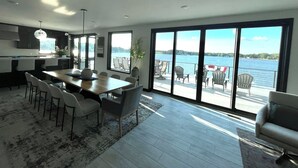 A modern kitchen with a dining area, large sliding glass doors to a balcony overlooking a body of water. - Luxury 6BR Round Lake Home Pool, Dock, Fire Pit & Stunning Sunsets!. (Dowagiac)