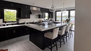 A modern kitchen with a large island, dark cabinetry, and pendant lighting. - Luxury 6BR Round Lake Home Pool, Dock, Fire Pit & Stunning Sunsets!. (Dowagiac)