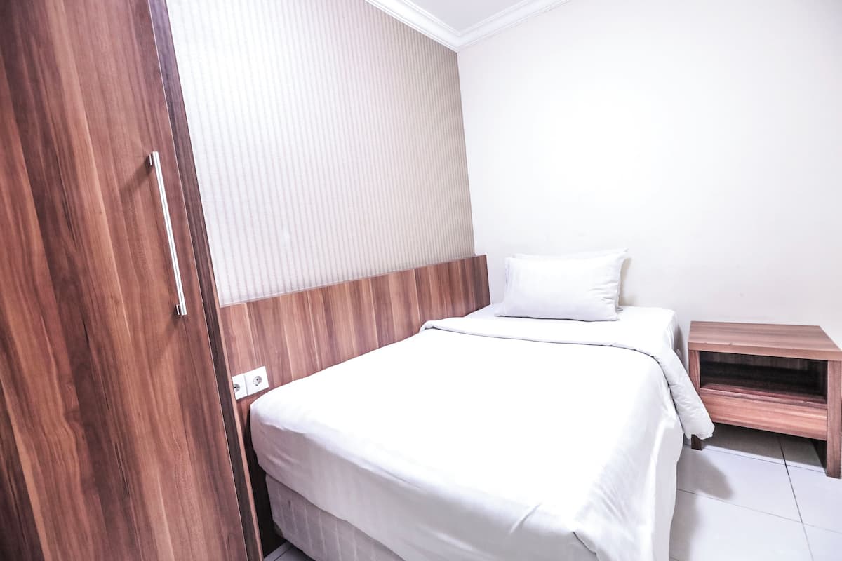 A bedroom with a wooden wardrobe, a bed with white bedding, and a small wooden nightstand.