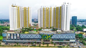 Un edificio residencial alto con varios balcones, una plaza central con techo a cuadros y zonas verdes circundantes.