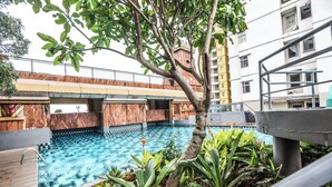 Una piscina con muelle de madera, rodeada de plantas tropicales, y un puente sobre el agua.