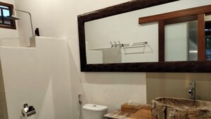 Une salle de bain comprenant des toilettes, un lavabo avec un meuble-vasque en bois, un miroir au-dessus du lavabo et une pomme de douche.