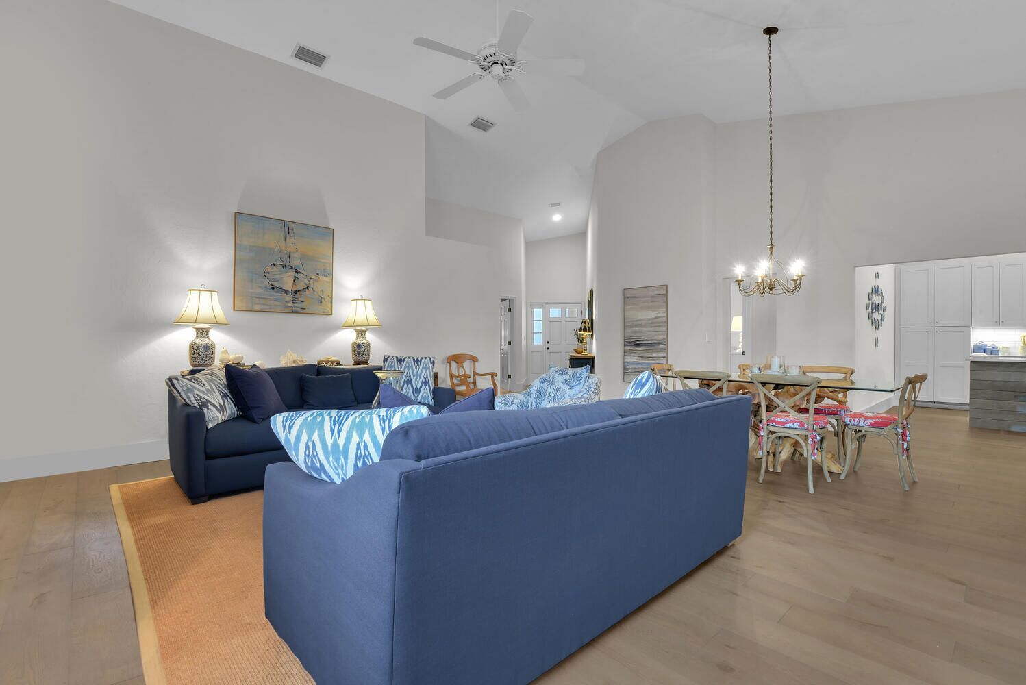 A spacious living room with a large blue sofa, a dining area with a table and chairs, and a kitchen in the background.