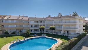 Ein mehrstöckiges Hotel mit Schwimmbad, Liegestühlen und viel Grün.