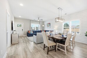 Uma sala de estar moderna com um sofá azul, uma mesa de jantar para quatro pessoas e uma área de cozinha com frigorífico e pia.
