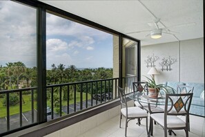 A balcony with a glass table, chairs, a potted plant, and a ceiling fan.
