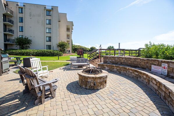 An outdoor patio area with Adirondack chairs, a stone fire pit, and a wooden fence.