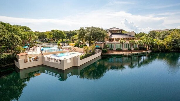 A resort with a pool area, a large building, and a body of water.