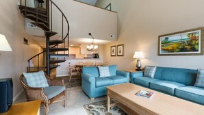 A spacious living area with a blue sofa set, a wooden coffee table, and a spiral staircase leading to an upper level.